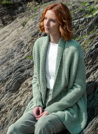 Red headed model sitting on rock wearing a sage green knitted kilcoole textured coatigan